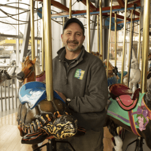 photo of Vin, the Senior Land Care Manager at Mill River Park in Stamford, Connecticut -- standing on a carousel 
